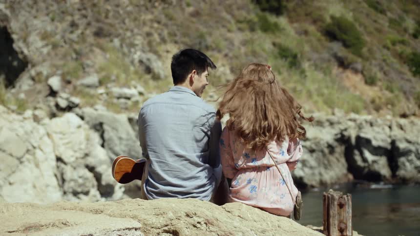 A man and woman sit on a rock near the ocean