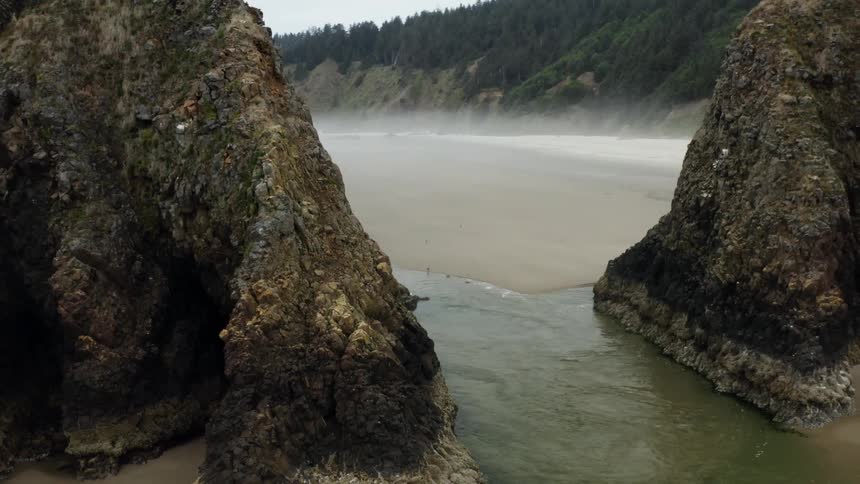 Several people are wading into the water at a sandy shoreline that is adjacent to a pair of cliffs that are made of very jagged rocks