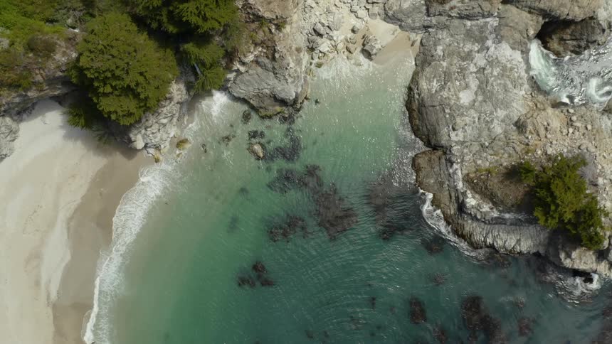 Aerial view of gentle waves crashing at the shoreline in a cove