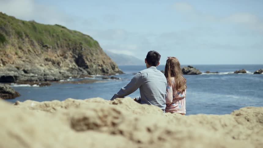A man and a woman sit on the shore watching the water