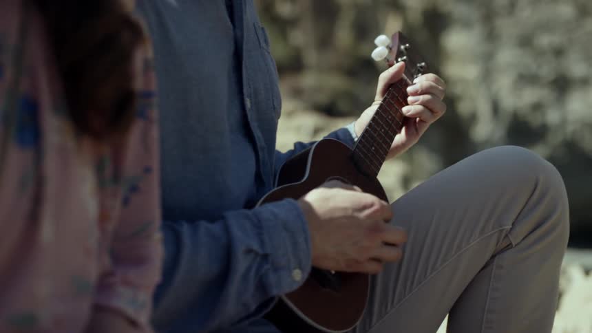 A man and woman sit and laugh while the man plays a ukulele