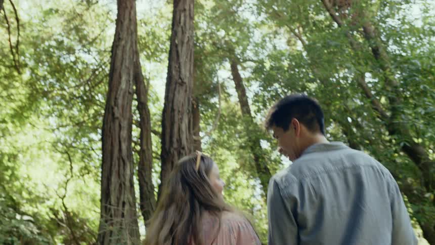 Asian man and white woman holding hands walk on the forest track in the woods during daylight