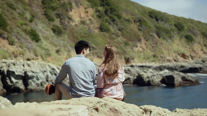 A man sits next to a woman on rocks overlooking a river