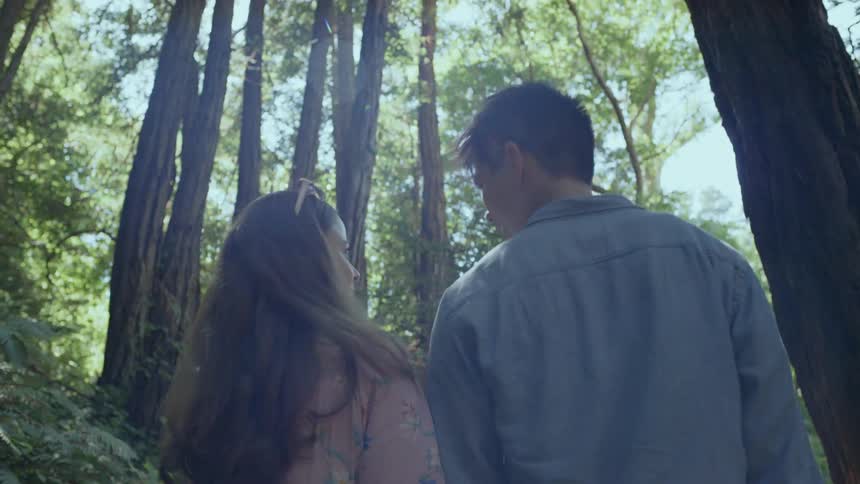 Asian man and white woman holding hands walk on the forest track in the woods during daylight