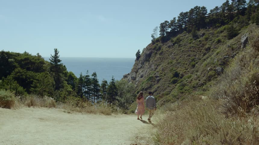 A man and woman walk along a path in the hills