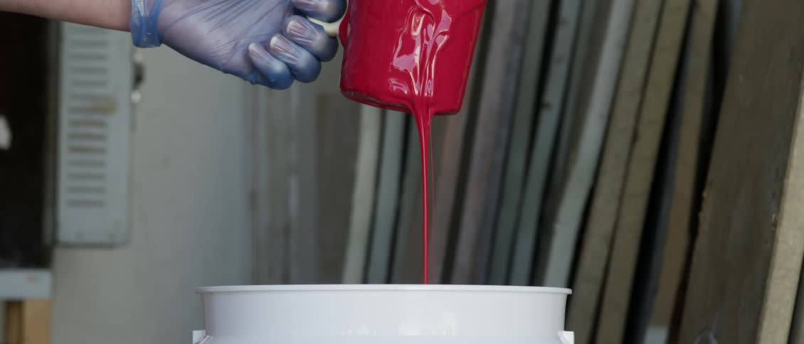 A gloved hand pours red paint from a coffee cup