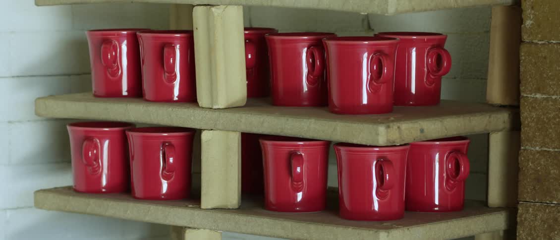 A cabinet door is opened to reveal red mugs