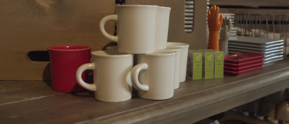 View of coffee cups, trays, small boxes and colored glass hands sitting on a shelf