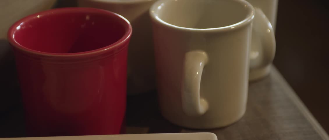 A red coffee mug rests next to white mugs