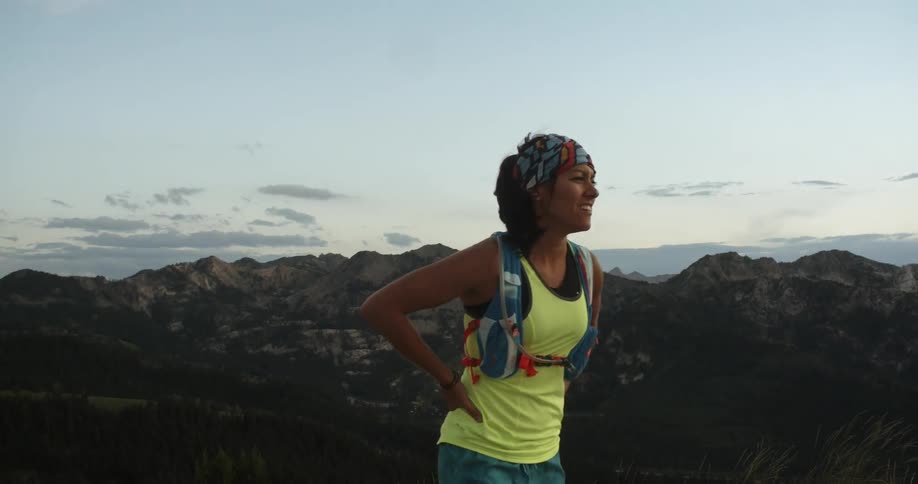 A woman jogging in the mountains before she stops and looks out over mountain peaks