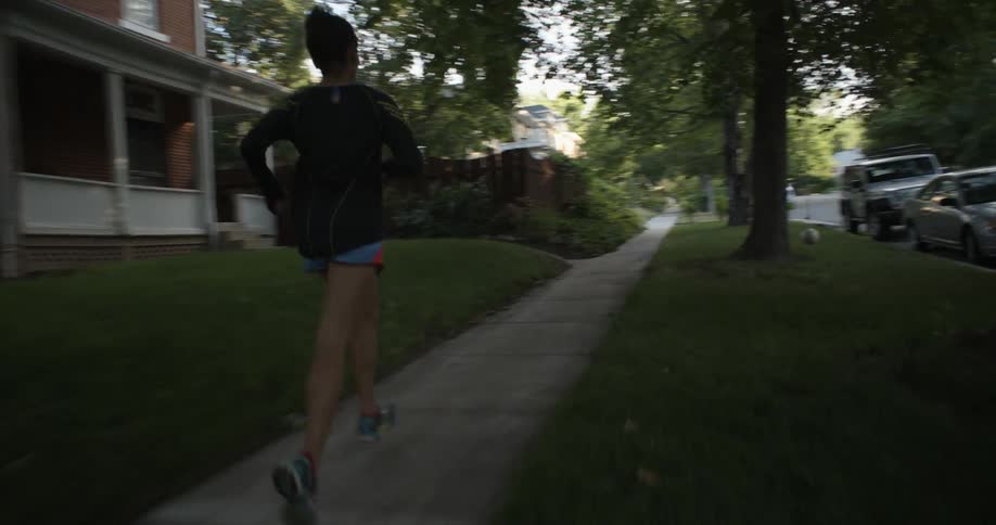 A woman jogs down the sidewalk in a neighborhood
