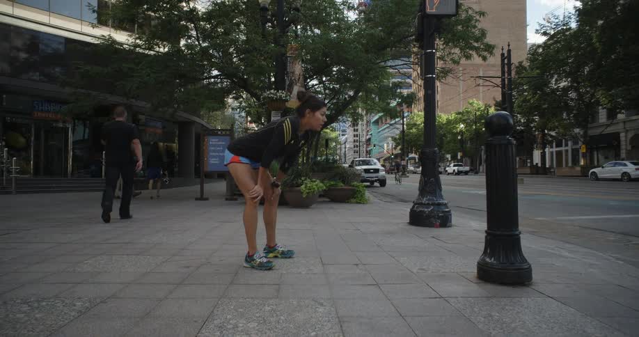 A woman stretches on the sidewalk on a sunny day