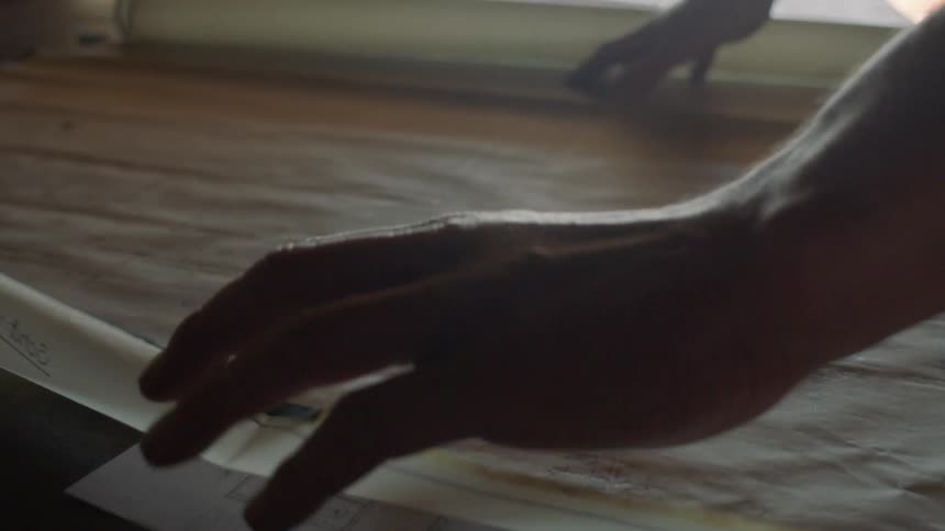 A person rolling out an architectural design onto a table