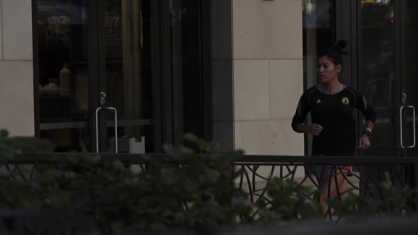 A woman runs on a sidewalk by a large building