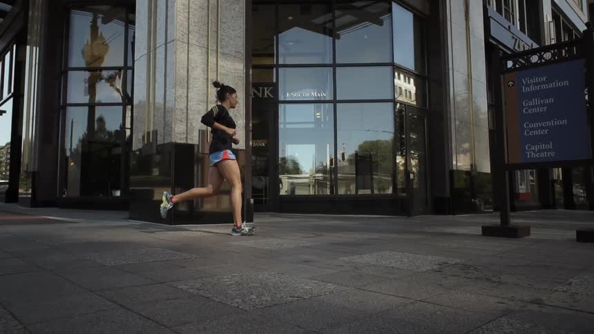 A woman jogs on a city sidewalk next to a city building