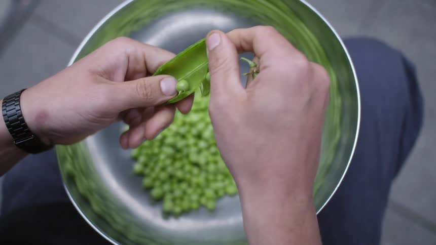 A person husks peas into a bowl