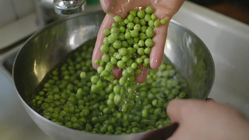 A white male stirs peas around in water in a bowl with his hand
