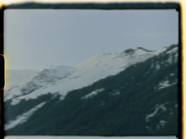 The camera pans a view of a mountain range in vintage footage