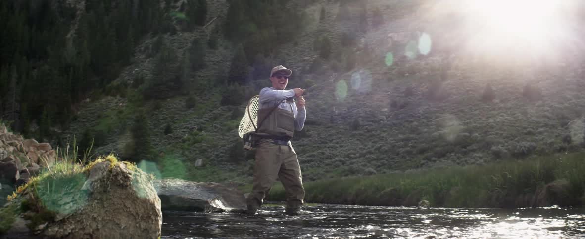 A man is fly fishing in a stream on a sunny day