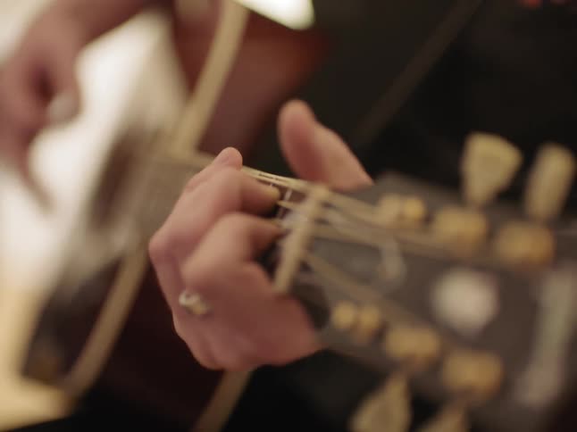 A white musician plays an acoustic guitar