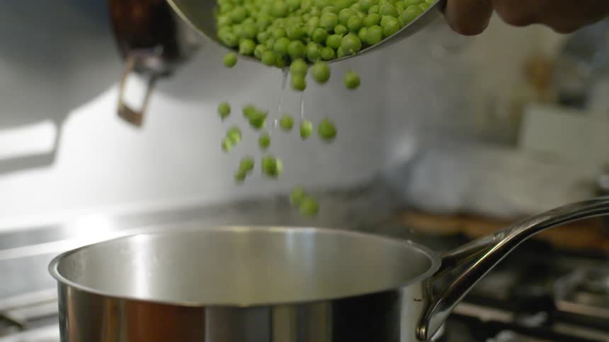 A cook pours fresh peas into a pot of boiling water on the stove