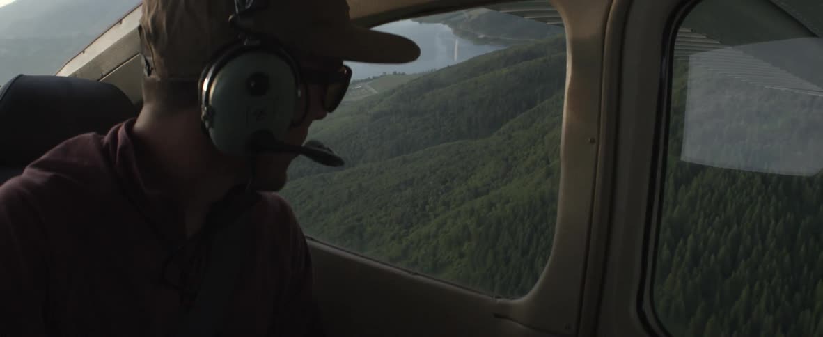 A person is looking outside of a plane window on some mountains