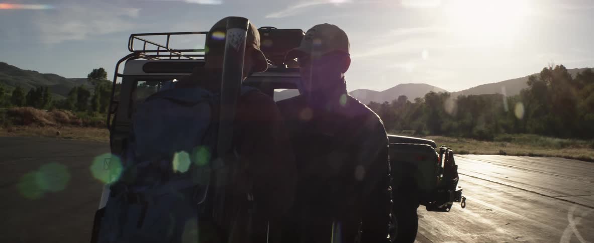 Two people greet each other by a vehicle on a sunny day
