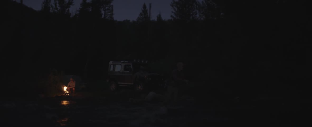 At night one man fishes and another sits beside campfire