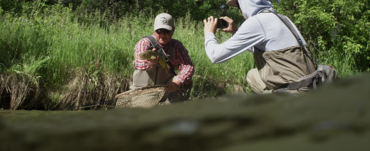 A man pulls a large fish from a net while another man photographs it