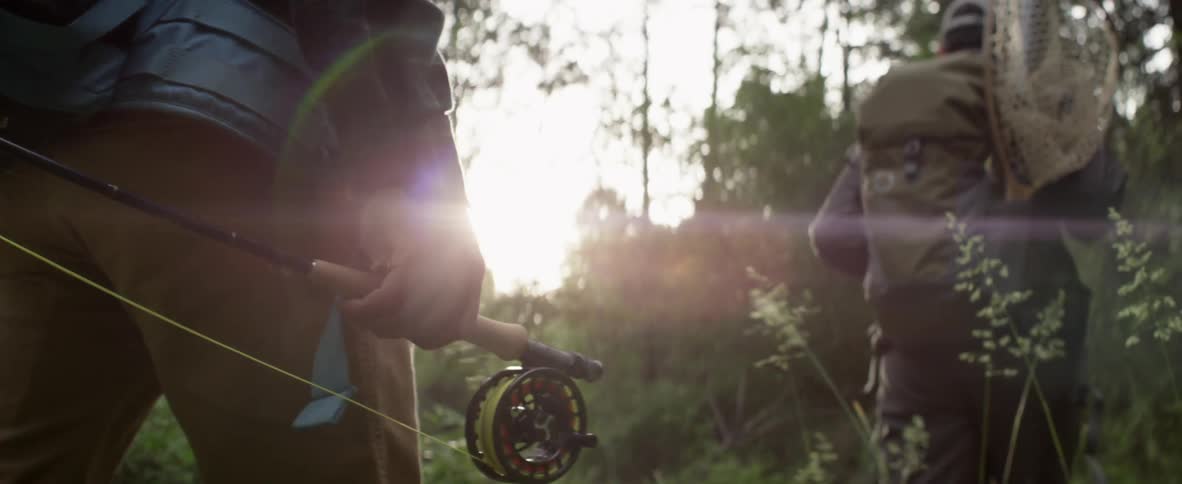 Men walking through the woods while holding fishing gear