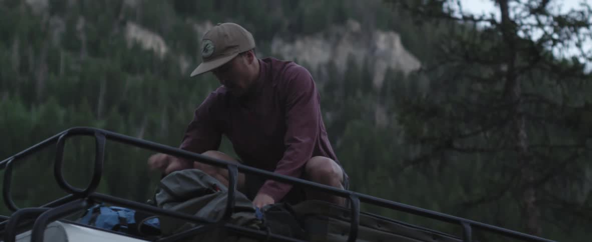 Man secures his camping gear to the top of his vehicle