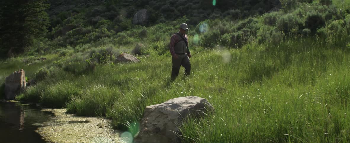 A man with a fishing pole walks across grass