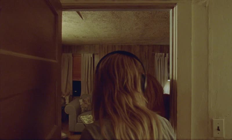 A young woman listening to headphones rising from her seat to open a door and walk around the woman on the other side