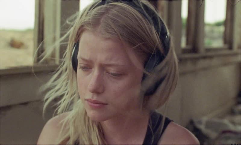 A girl wears headphones as she sits in a run down abandoned building and the wind blows through her hair