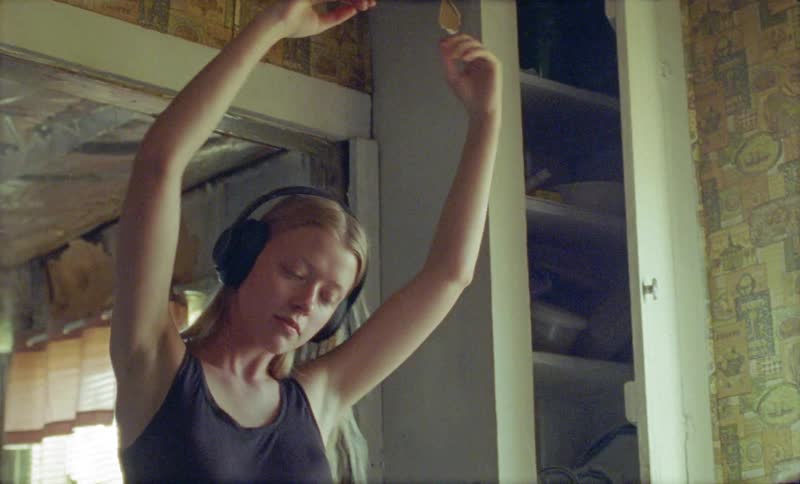 Blonde woman wearing headphones dances in a room during daylight