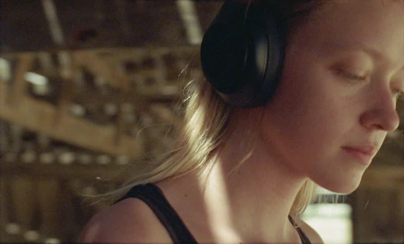 Blonde girl wearing headphones walks in a hut in the forest during daylight