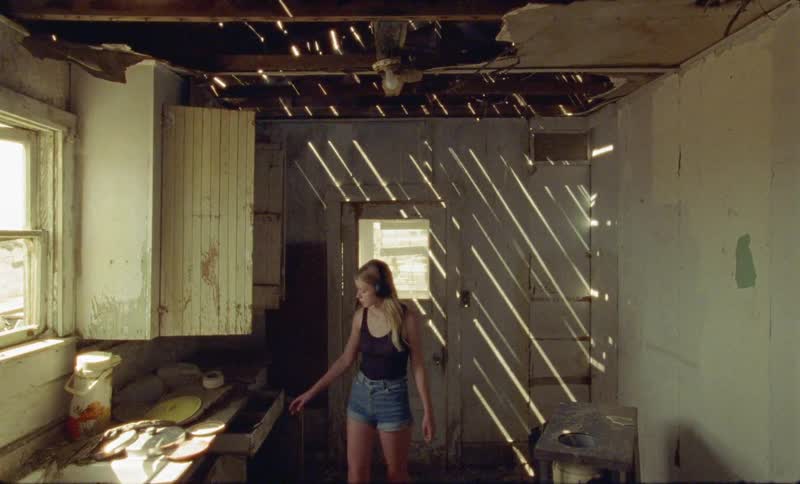 A young woman wearing headphones entering a dilapidated kitchen