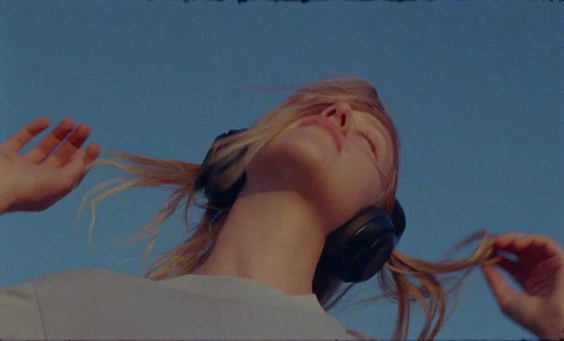 Blonde woman wearing headphones listens to music and dances under blue sky