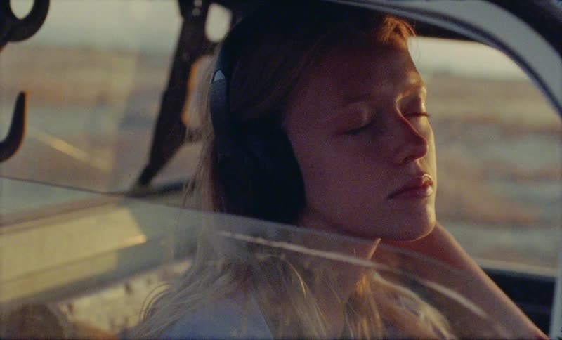 A woman wearing headphones sitting in a car sways to the music with eyes closed