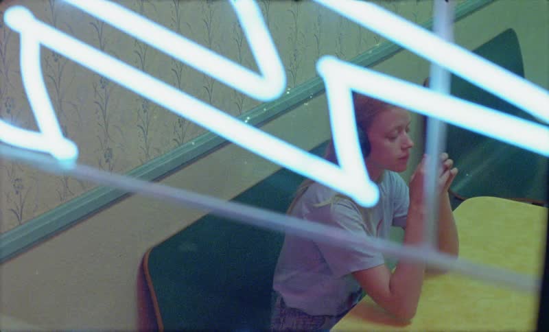 A worried looking young woman wearing headphones sitting at a table in a diner