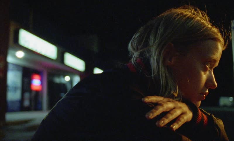 An upset woman sits outside a convenience store at night