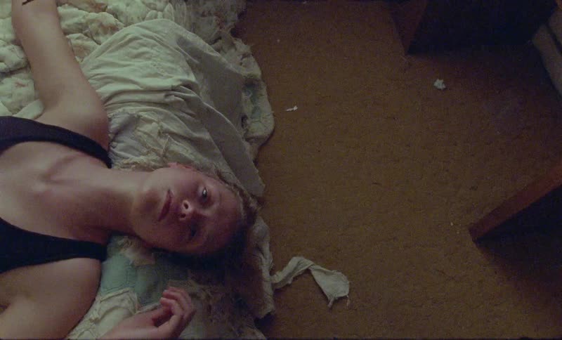 A caucasian woman with sandy colored hair lays on a mattress on the floor while she looks at the ceiling