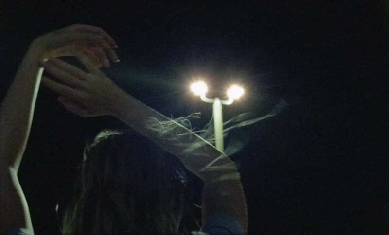 A young woman slowly dancing outdoors at night while listening to a pair of headphones
