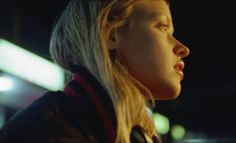 Blonde girl looks ahead and wears headphones outside at night