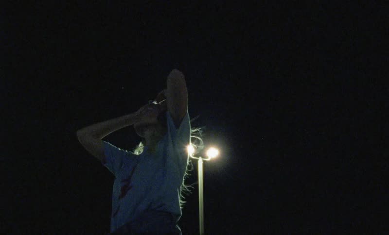 A young woman standing outdoors at night slowing dancing while listening to a pair of headphones