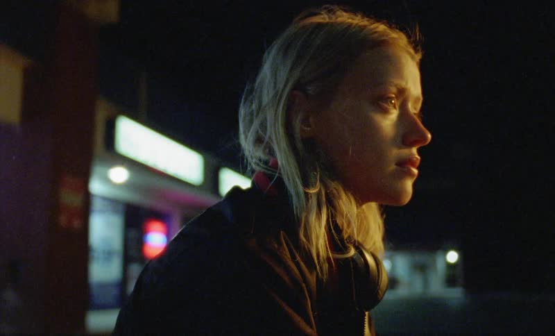 A sad woman sits outside a convenience store at night