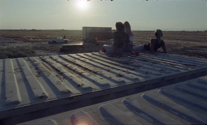 Three people sit on a roof and watch another ride a dirt bike