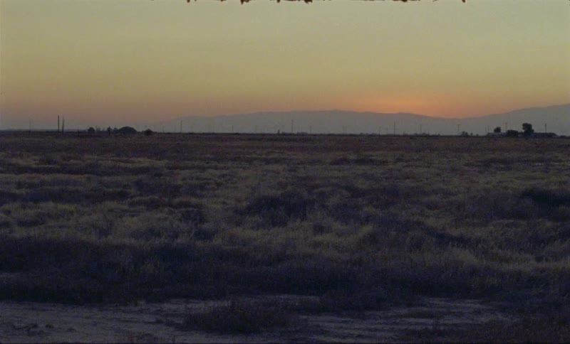 The sun sets behind mountains in a rural setting