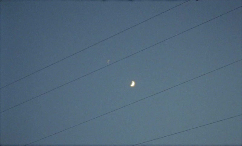 The moon shines in the daytime sky behind power lines that obscure the view