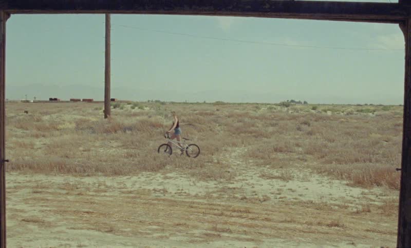 A girl pushes her bicycle through the desert